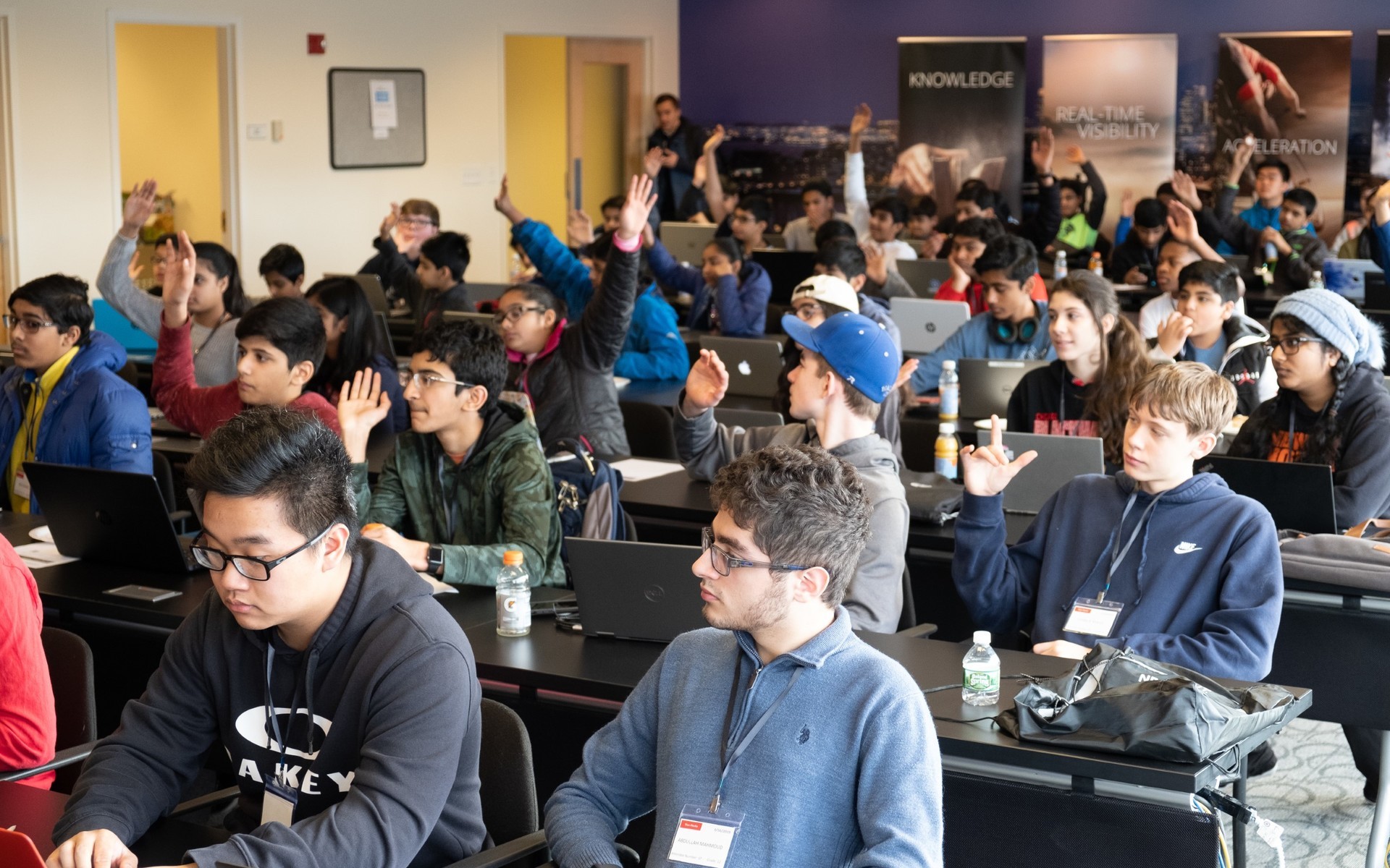 A group of students sitting in a large conference room, some with their hands raised